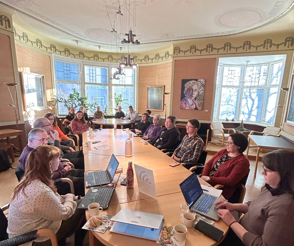 Kuvassa kokoustetaan isolla joukolla pitkän pöydän ääressä.