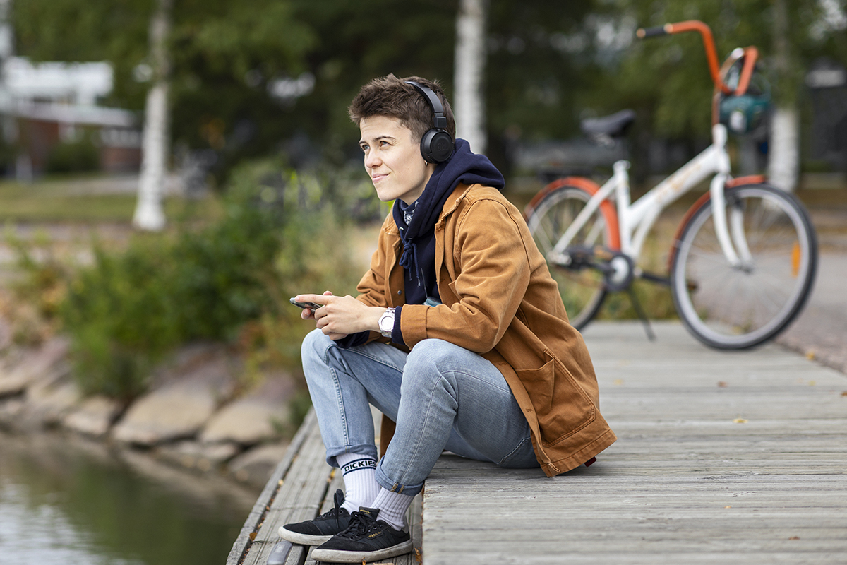 Henkilö istuu laiturilla ja kuuntelee äänikirjaa