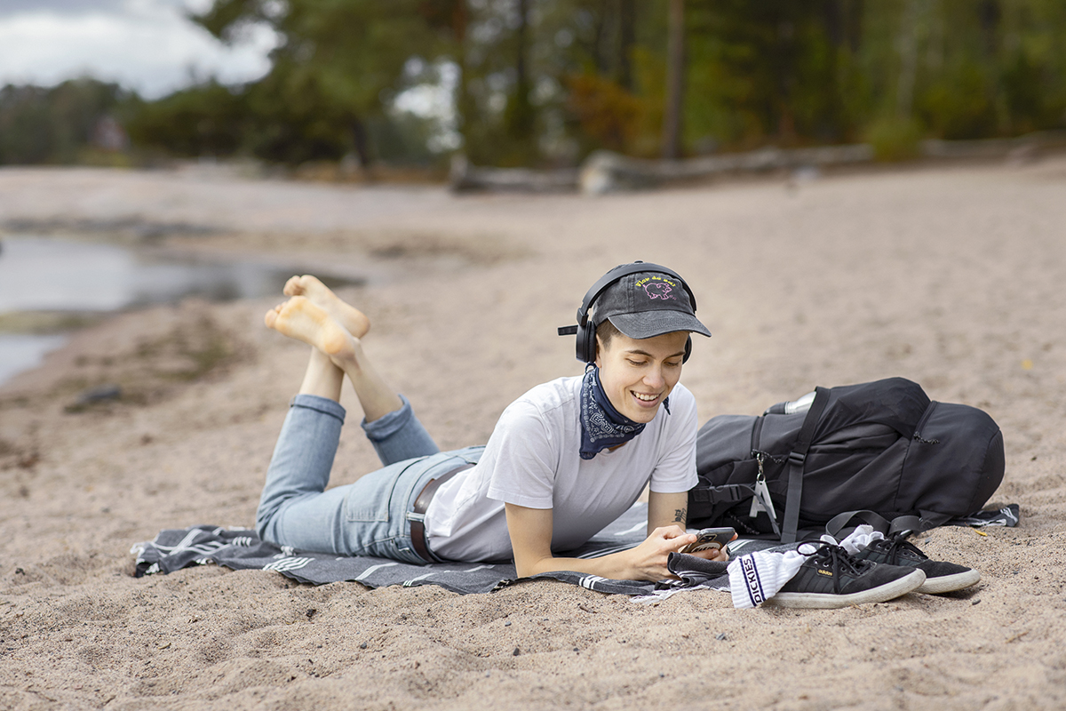 Henkilö makailee hiekkarannalla ja kuuntelee e-kirjaa